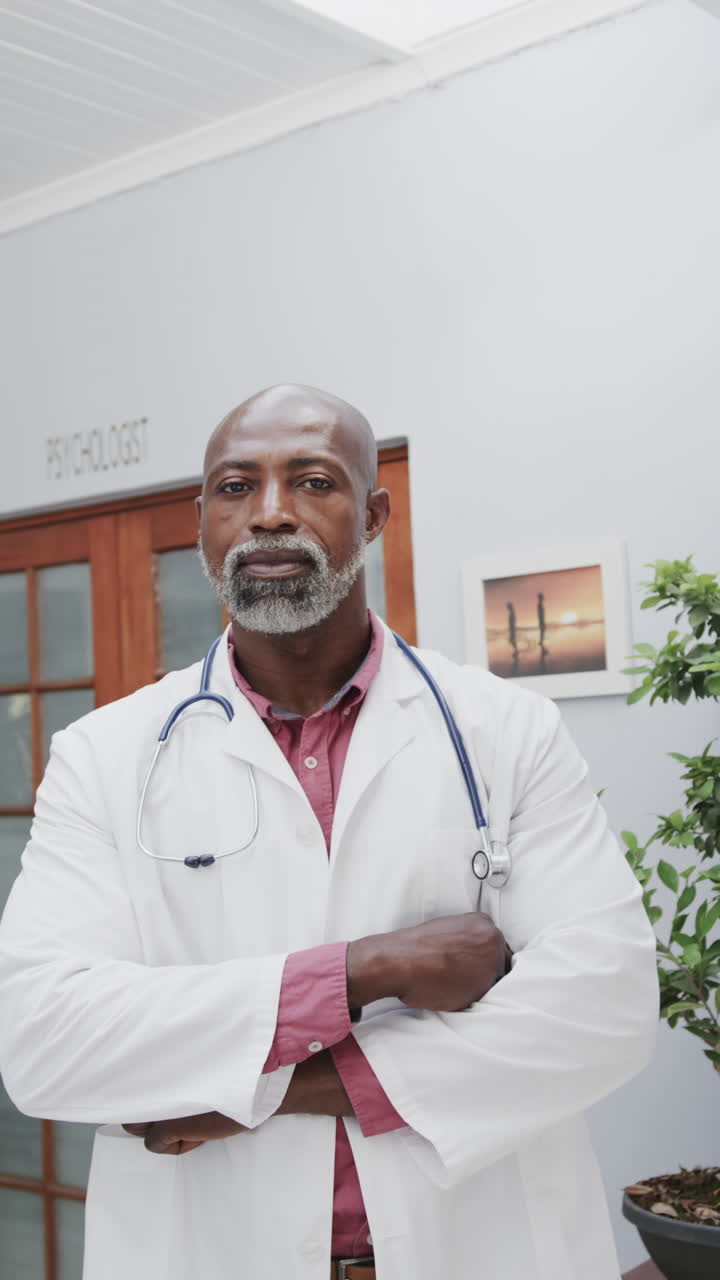 Vidéo verticale en portrait d'un médecin afro-américain, les bras croisés et souriant, au ralenti