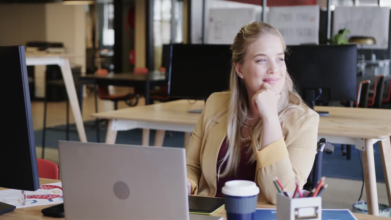 Glad kaukasisk afslappet forretningskvinde i kørestol, der bruger bærbar computer på kontoret, i slow motion.