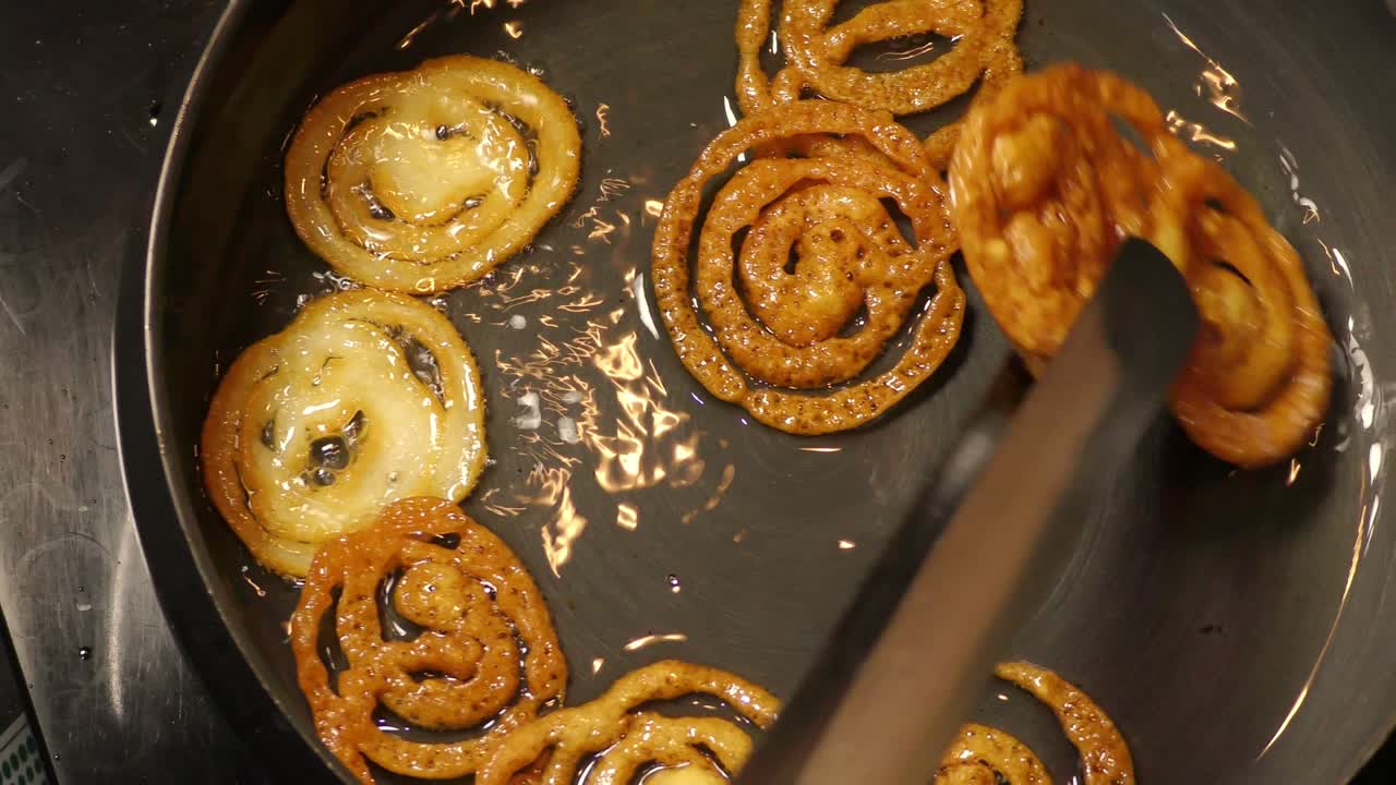 freír y recoger pedazos de jalebi marrón en aceite calentado en la sartén