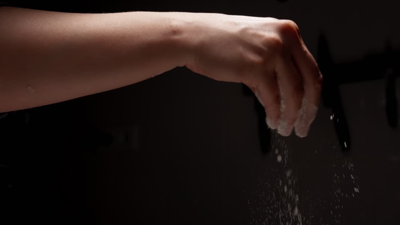 Primo piano di una mano che sparge farina su sfondo scuro