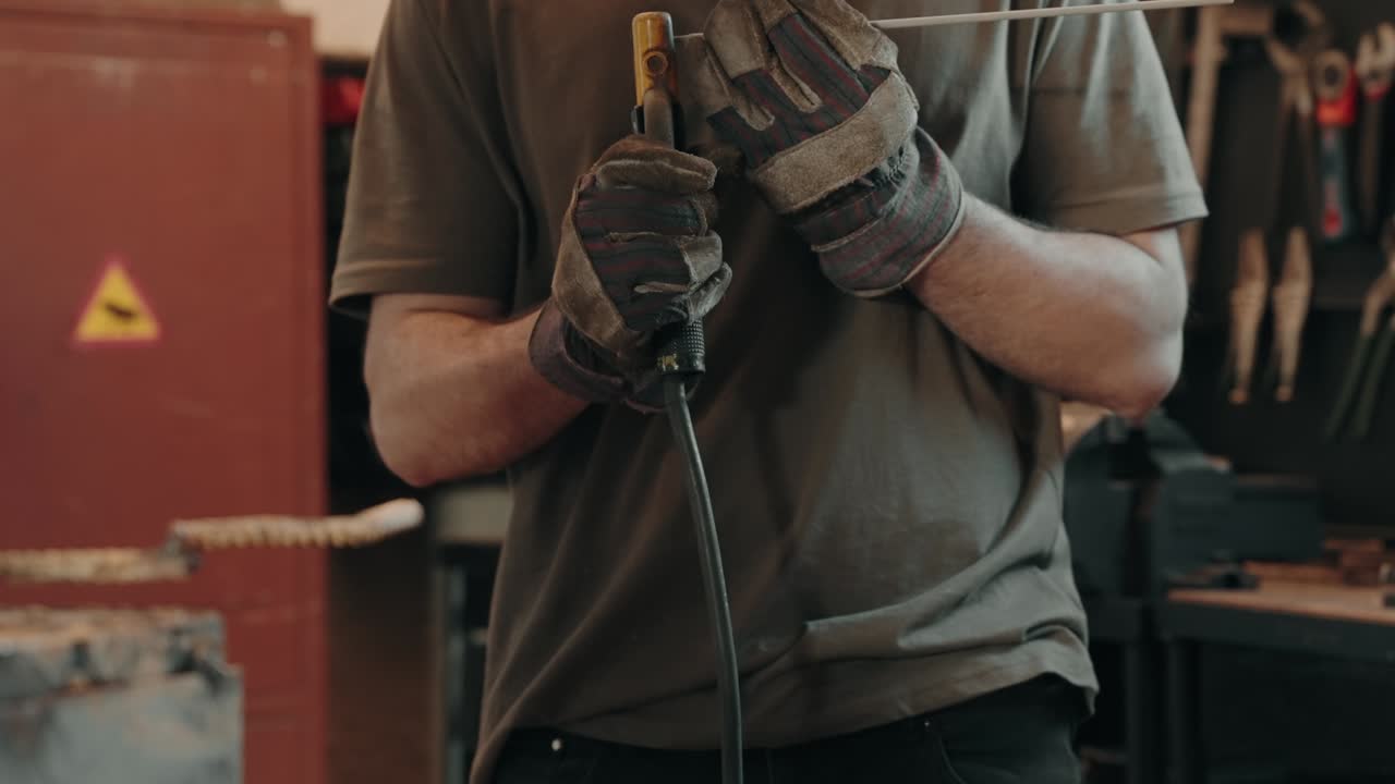Man holding welding rod with gloves preparing for metalwork indoors - slow motion