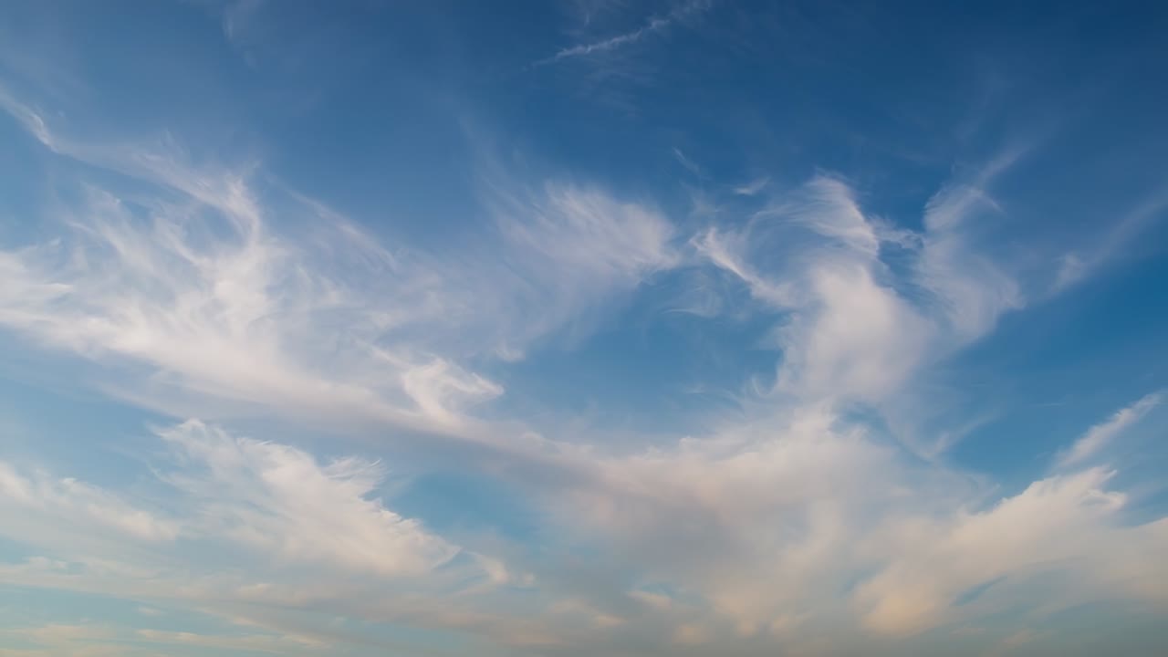 Drevet af vind i de øvre luftlag ses en cirrus-fjer, der langsomt flytter sig hen over eftermiddagshimlen med kondensstriber