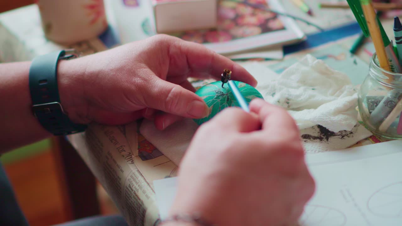 primer plano medio de un artista dibujando diseños ornamentados tradicionales en un huevo de pascua verde