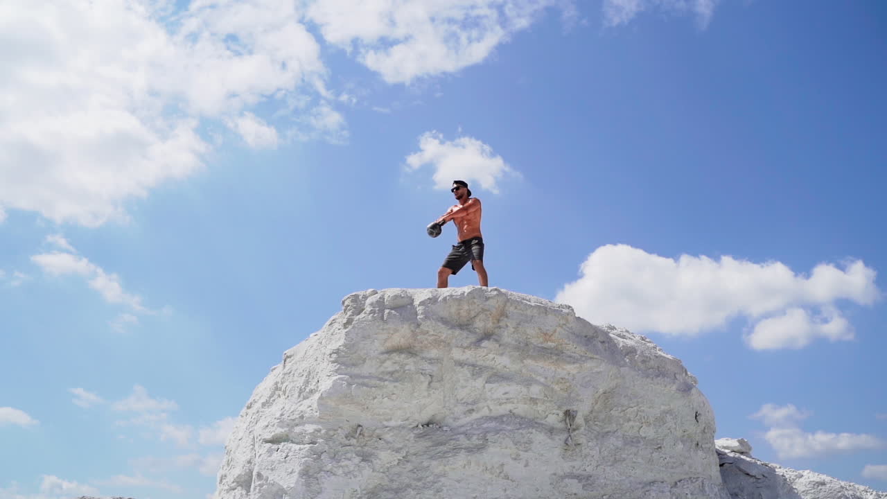 Fitness training man lifting heavy kettlebell weight. Muscular man lifts weight on the top of high hill. Cross training outdoors.