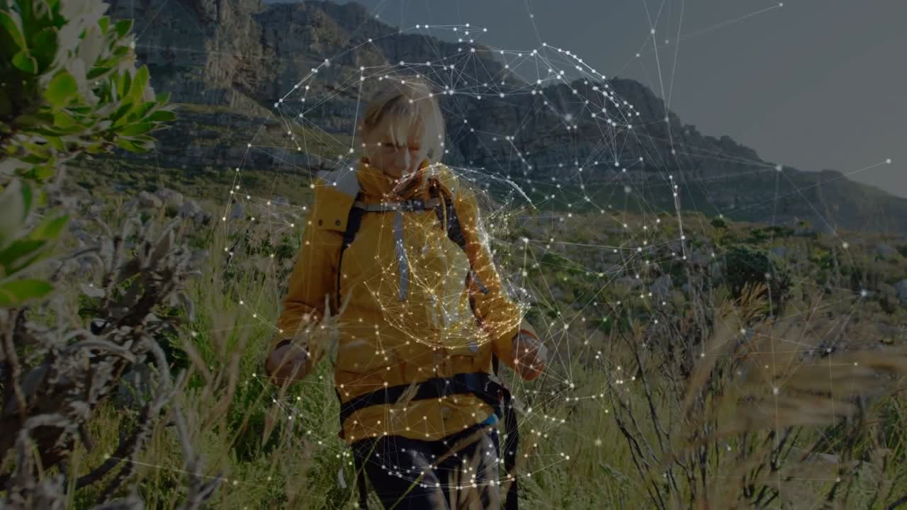 Escursionista che cammina su un sentiero di montagna, facendo un passo avanti, con una sfera a rete che cresce intorno al busto mostrando tecnologia.