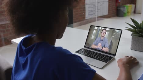 Back-view-of-african-american-woman-having-a-video-call-on-laptop-with-male-colleague-at-office