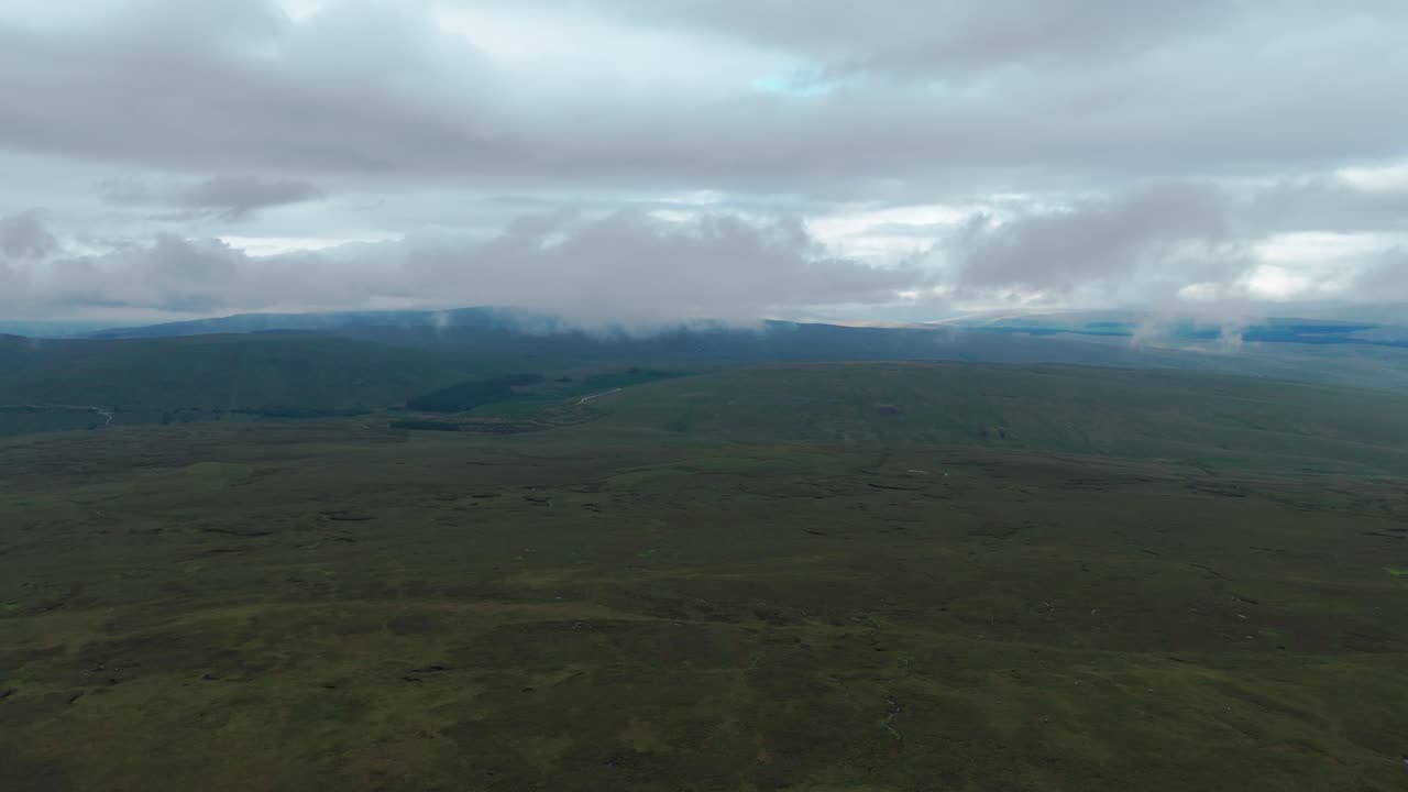 vasto paisaje verde bajo cielos nublados con colinas distantes y atmósfera brumosa, vista aérea