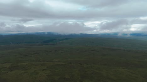 vast green landscape under cloudy skies with distant hills and misty atmosphere, aerial view