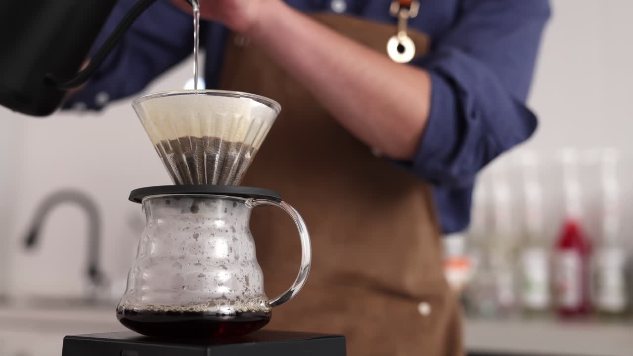 Professioneller Barista bereitet Kaffeegetränk im Drip- oder Filterpapier-Stil zu, indem er die Pour-Over-Methode anwendet und heißes Wasser gießt, um ein koffeinhaltiges Getränk aus Kaffeebohnen in einem Café-Restaurant zuzubereiten.