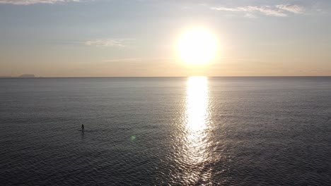vista aérea de un paddle boarder en medio del océano al amanecer