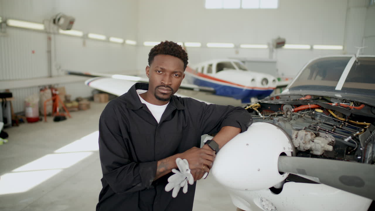 Retrato de mecânico de aeronaves negro em pé ao lado de um avião no hangar.