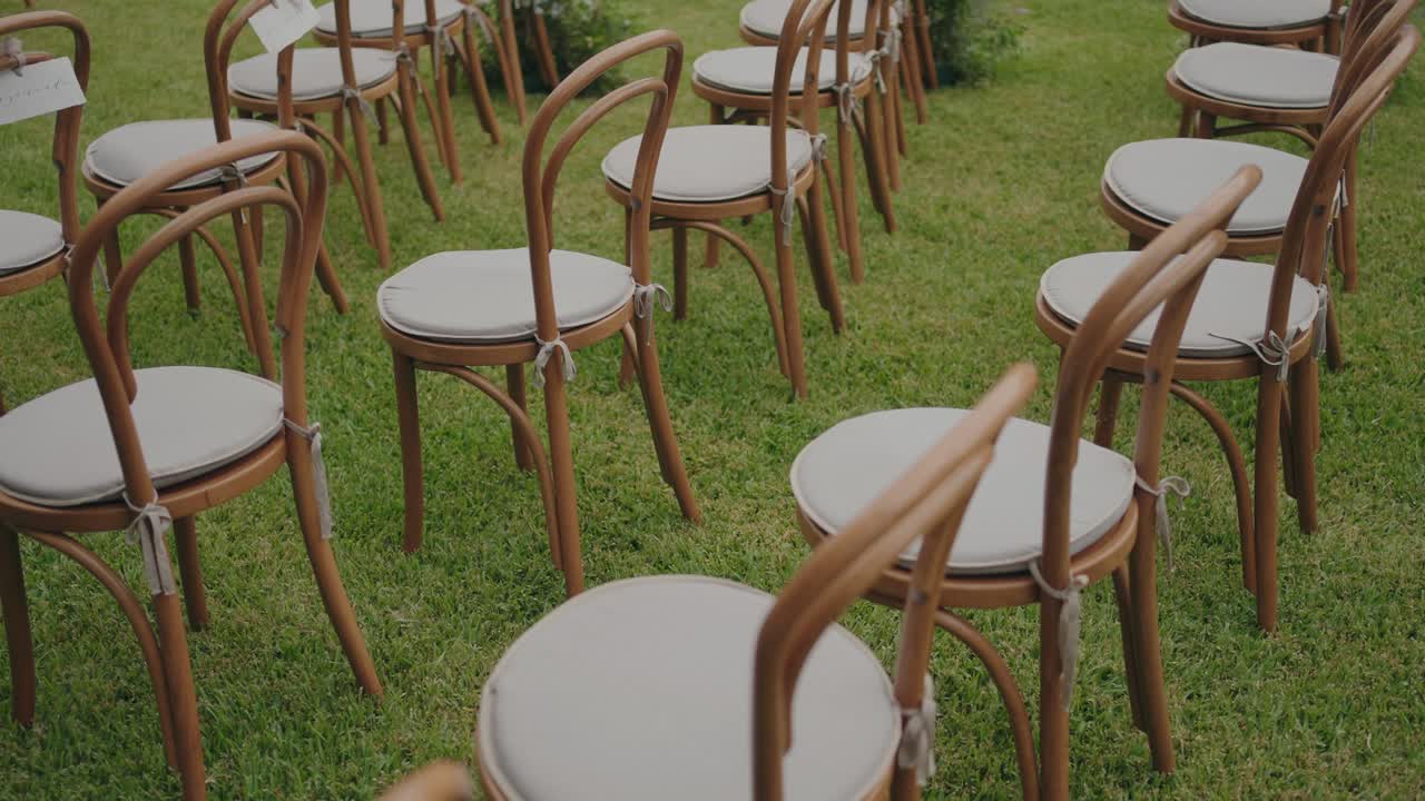 Wooden chairs with white cushions neatly arranged outdoors for a ceremony or gathering