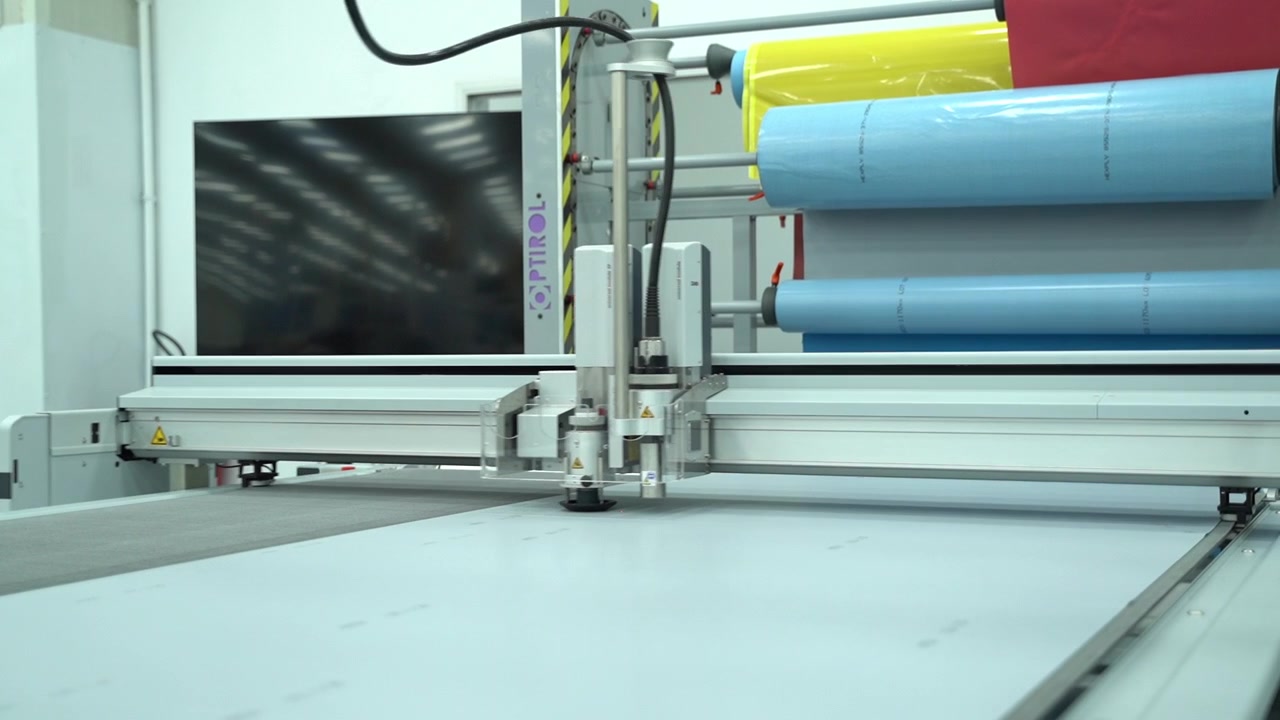 Tavolo da taglio automatizzato con un operaio e rotoli di materiale nelle vicinanze.