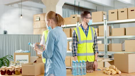 caucasian young male and senior female volunteers in facial mask giving food and water to homeless people in charity warehouse