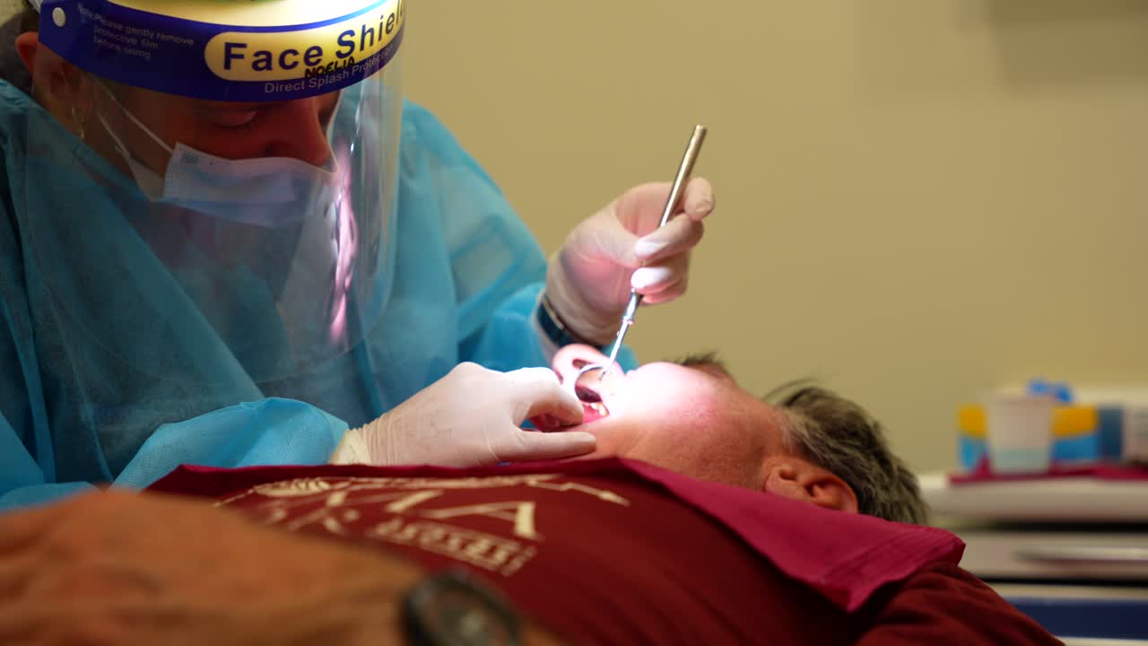 Dentista che esegue una procedura su un paziente che indossa visiera protettiva e guanti