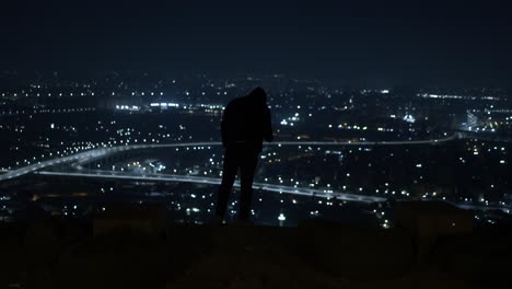 man in black jacket standing on a top view overlooking the expressway at midnight