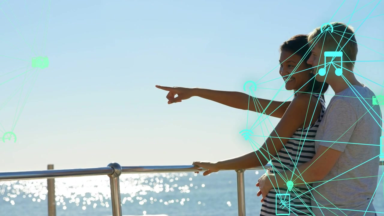 Woman on rail to sea raising arm pointing man holding turquoise tech icons growing around couple