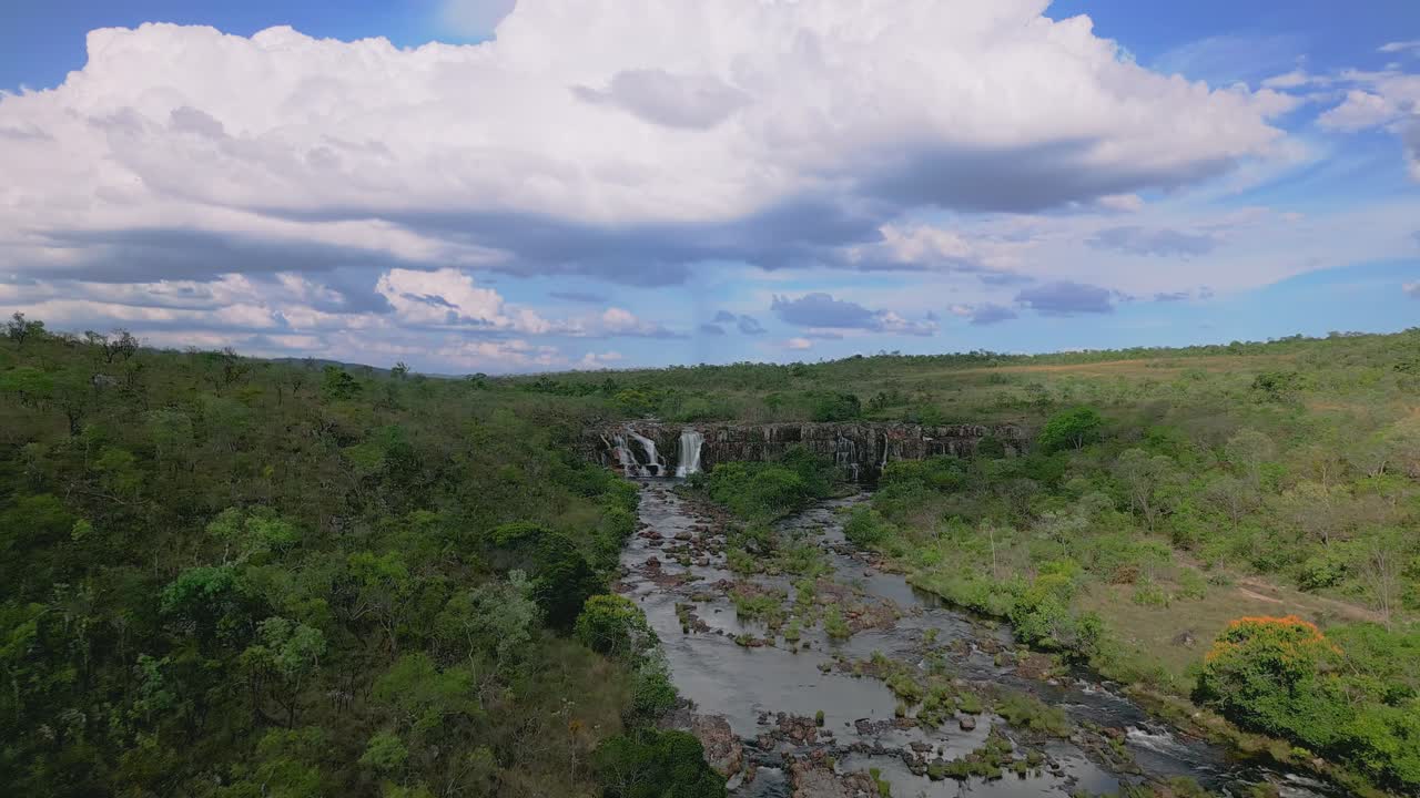 Water flows over rocks, forming dos Couros waterfalls and rapids, under a partly cloudy sky in the brazilian Cerrado at Chapada dos Veadeiros national park in Cachoerias, drone flying dorward