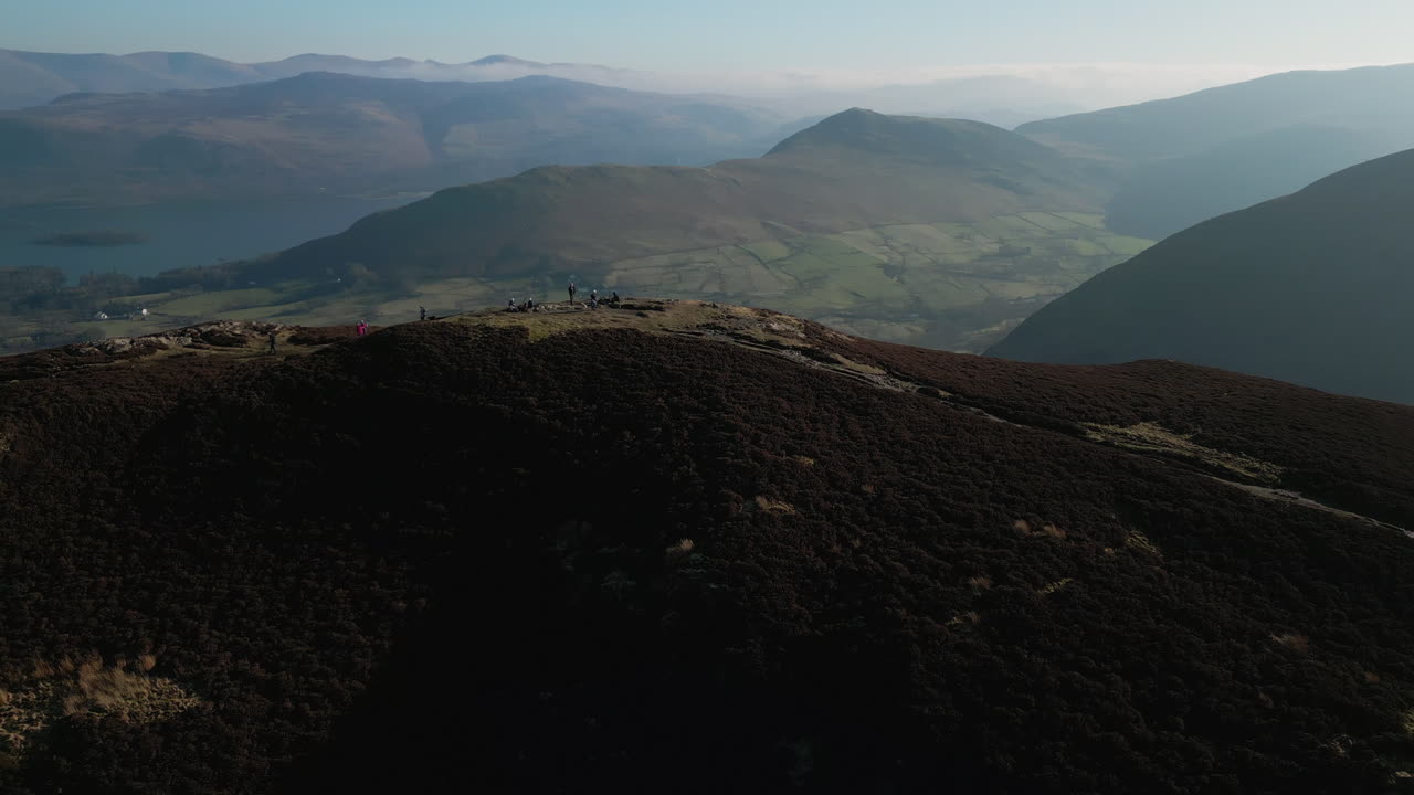 barrow fall lake district uk에서 자연 렌즈 플레어가있는 안개 낀 산과 녹색 계곡을 드러내는 궤도를 가진 산 꼭대기의 등산객