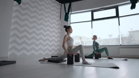 Two-women-in-the-background-of-the-window-do-a-stretch-in-a-sports-studio.-Stretching-exercises.-Women-do-health-exercises-from-Pilates