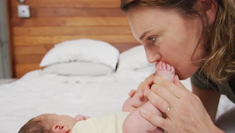 video of happy caucasian mother kissing feet of newborn baby