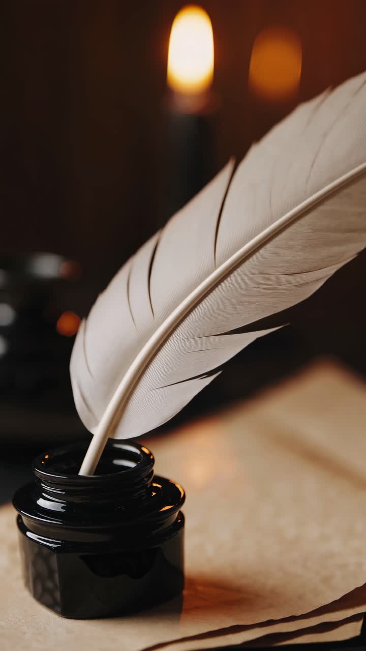 Close-up video of a quill in an ink pot on parchment, with warm candlelight in the background