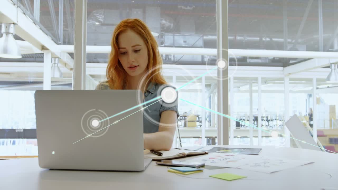 Donna che lavora al laptop in ufficio, il laptop lancia una sovrapposizione di dati che si allinea con i documenti per l'analisi.