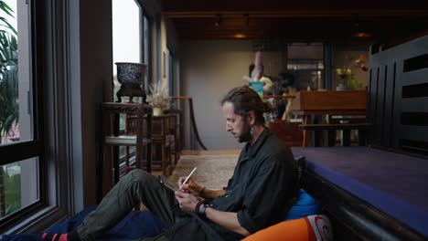 man drawing on tablet by window in a creative space