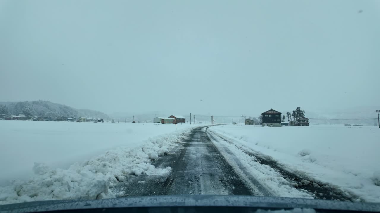 Snow lines the sides of a quiet road as a car travels through rural Japan