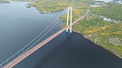 aerial view of vehicles crossing hogakustenbron bridge over tranquil sea and autumn forest in sweden