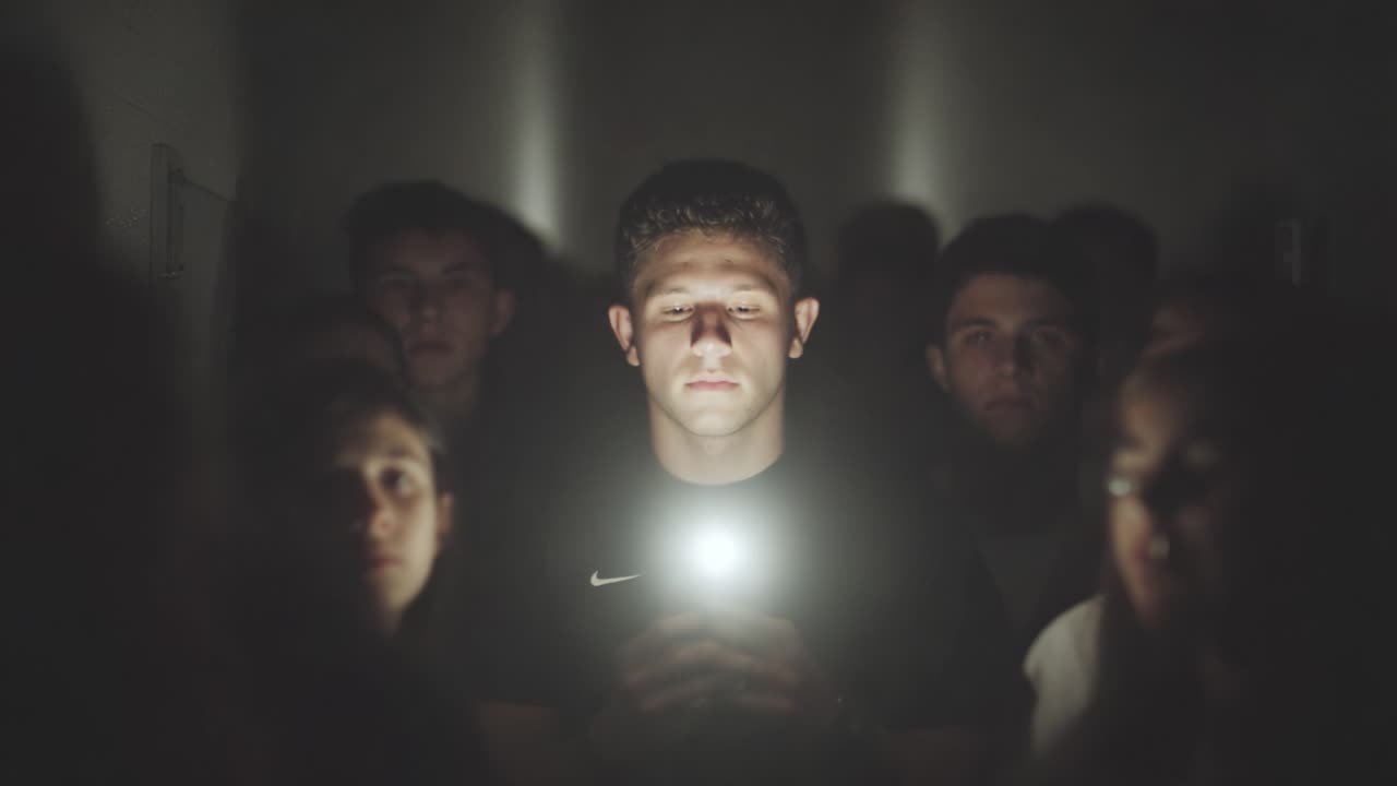 A Moment of Stillness: A Group Faces an Engaging Experience as One Individual Illuminates the Darkness with a Phone's Light, Creating an Atmosphere of Anticipation and Connection