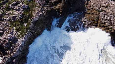 Big-wave-splash-as-it-crashes-into-jagged-rocky-coastline,-Hermanus