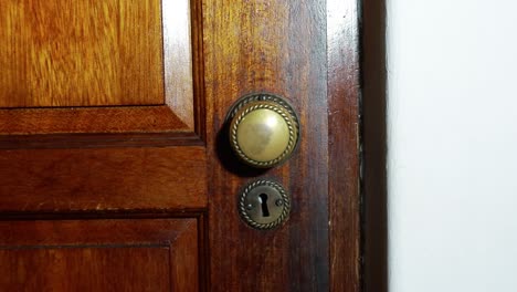 Door-knob-turns-and-man-with-black-glove-opening-wooden-door-slowly