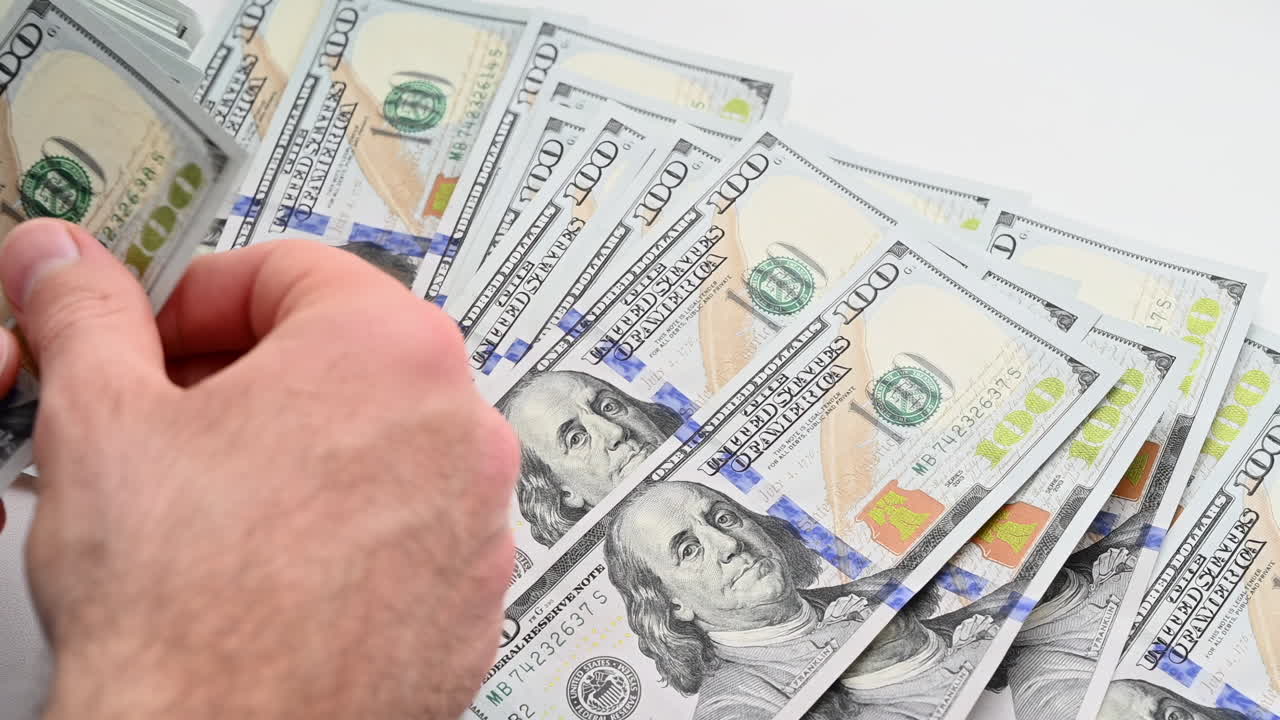 A man's hands quickly count a stack of one hundred dollar bills against a light background