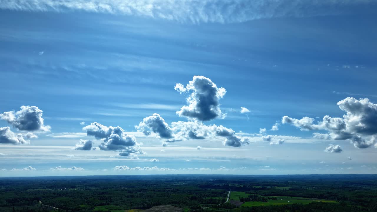 Hyperlapse from drone showing layered cloud formations over rural landscape in motion, smooth air in blue sky