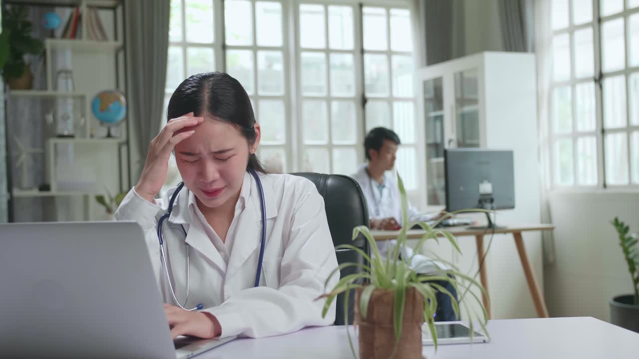 Young Asian Woman Doctor Is Using Laptop Computer And Headache In Workplace. Medical Concept