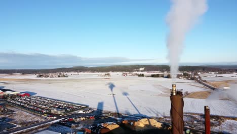 La-Chimenea-Emite-Una-Nube-Gris-Blanca-De-Humos,-Una-Larga-Sombra-Proyectada-Sobre-La-Nieve-Detrás-En-La-Región-Industrial