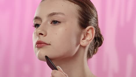 young woman using facial stone for skin care routine a young woman demonstrates a skincare routine using a facial stone tool set against a pink background