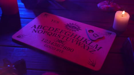 close up video of a wooden ouija board on a table surrounded by candles and a cross in a muffed - close up video of a wooden ouija board on a table. wax candles and a cross around. the planchette is slowly moving across the board, spelling out words and numbers. creative mystical content