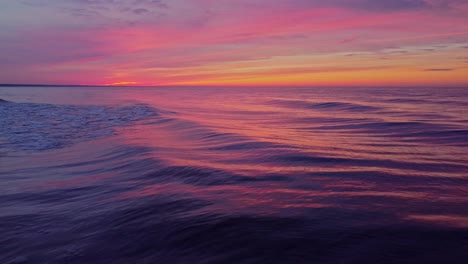 sea waves rolling and reflecting orange sunset sky, low altitude aerial