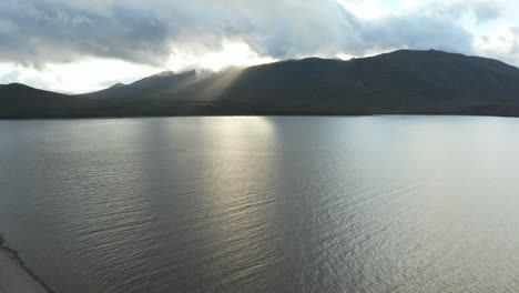 fly over aerial drone footage showcasing rays of light piercing through mountain range at lake te anau, new zealand