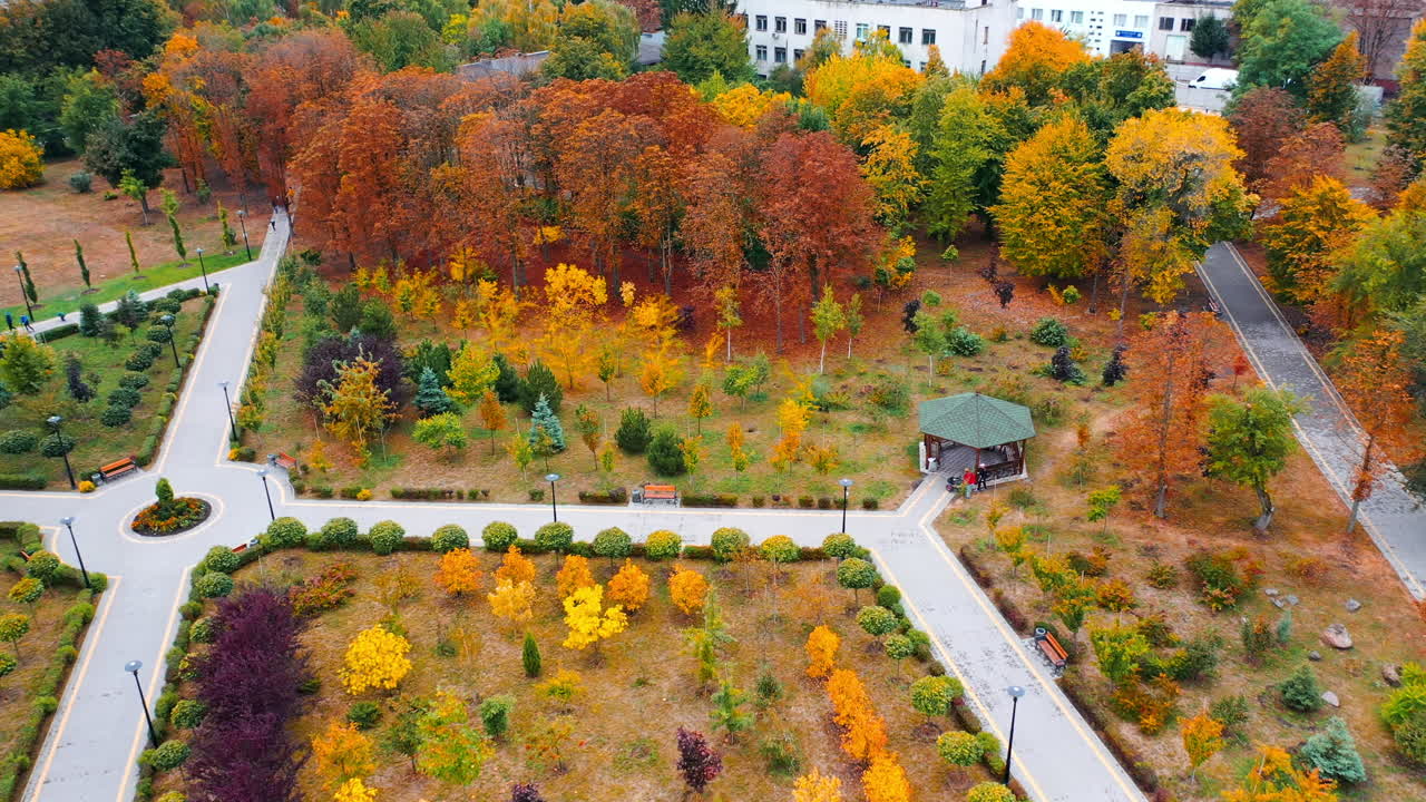 Lovely park with paved paths and pavilion among the bright trees. Drone footage over the peaceful beautiful area in the city.