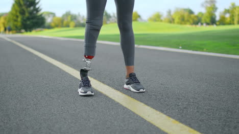 jogger with artificial limb standing in park. woman at start position on road