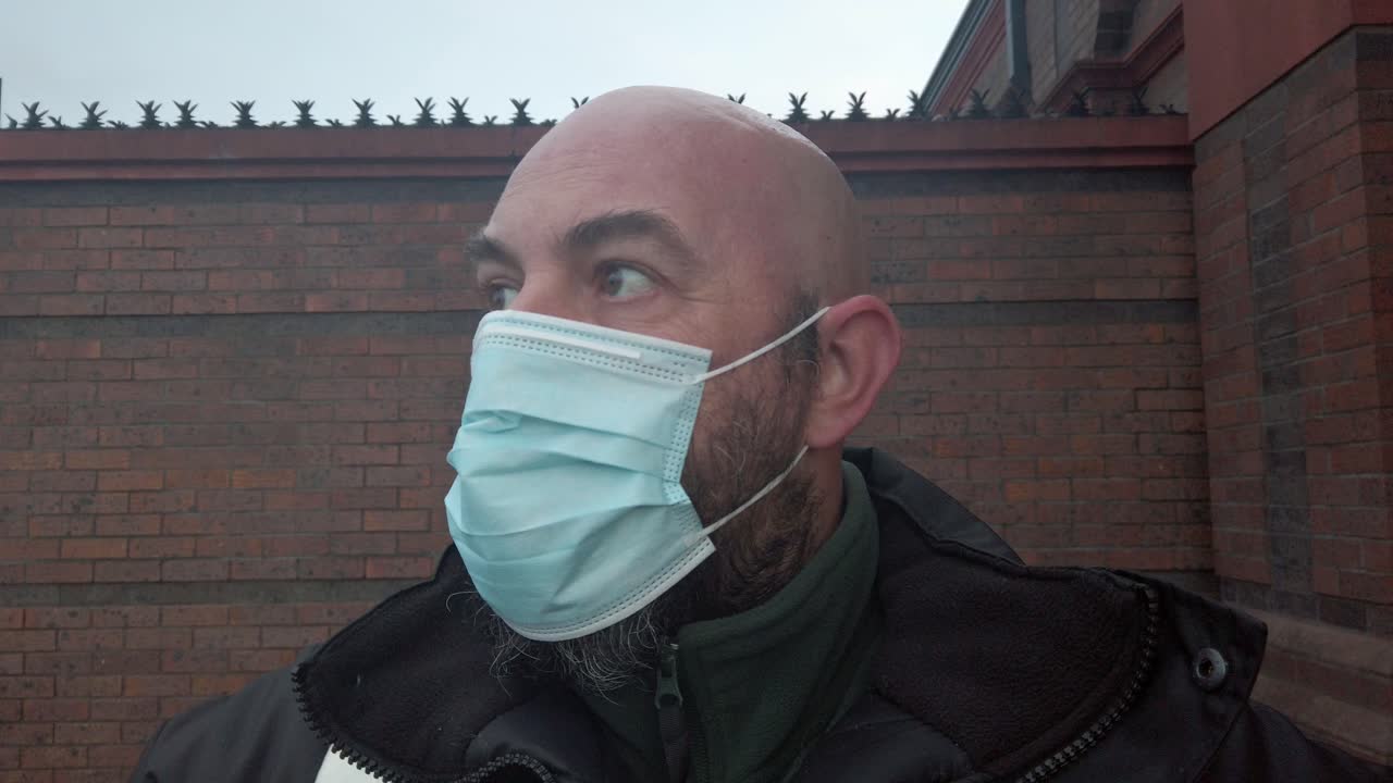 el guardia de seguridad masculino repara la máscara protectora de ppe médico del virus de la corona frente a una pared de ladrillo alta
