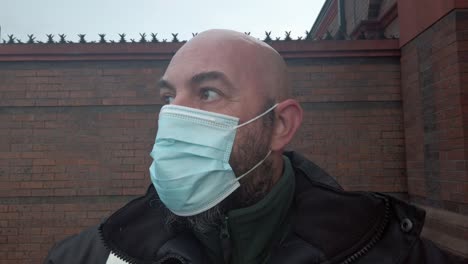 male security guard fixes protective corona virus medical ppe mask in front of high brick wall