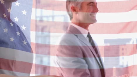 Waving-american-flag-against-mid-section-of-businessman-and-businesswoman-shaking-hands