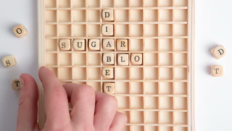 hand spelling out diabetes message in wooden dice on grid