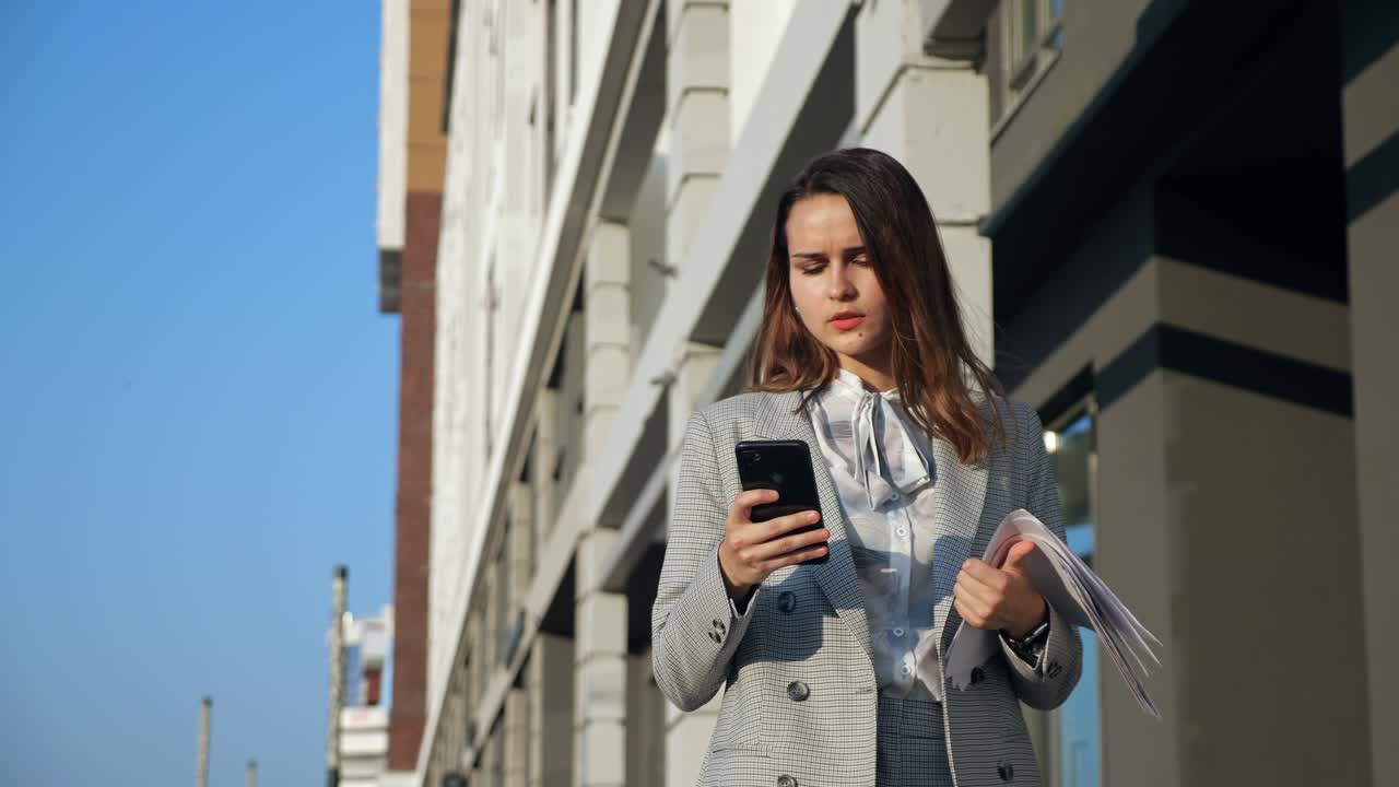 giovane donna in tailleur con un telefono e documenti che cammina per strada