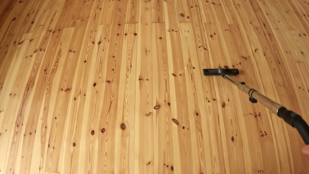 Handheld vacuum sweeping a polished timber floor from a wide overhead angle, showing clean lines, natural wood grain, and tidy home maintenance in progress