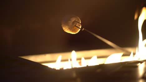 tasty white marshmallow on skewer roasting over gas fire pit